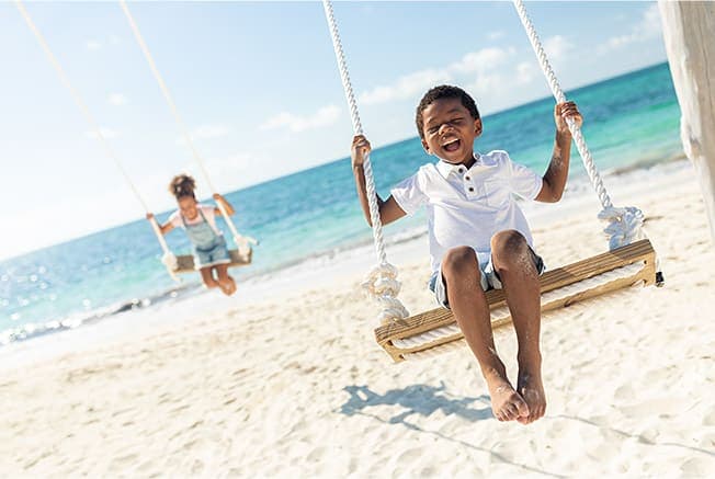 Young Boy And Girl On Swings At The Beach