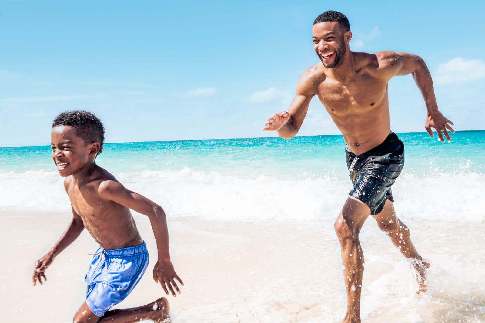 A father and son running along a white-sand beach in the Nassau and Paradise Island area